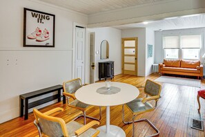 A room with a round table, four chairs, a bench, a sofa, a fireplace, and a door leading to another room.
