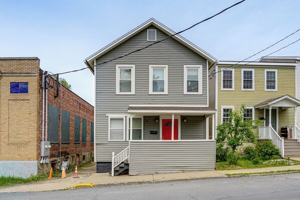 A two-story residential building with a red door, a front porch, and a brick wall adjacent to it. - Walk to Everything! Dtwn Hudson Apartment (Hudson)