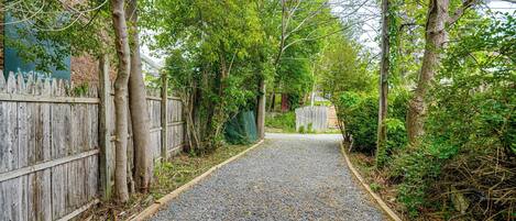 Un chemin de gravier bordé de clôtures en bois et d’arbres, qui mène à un bâtiment doté d’une porte verte.