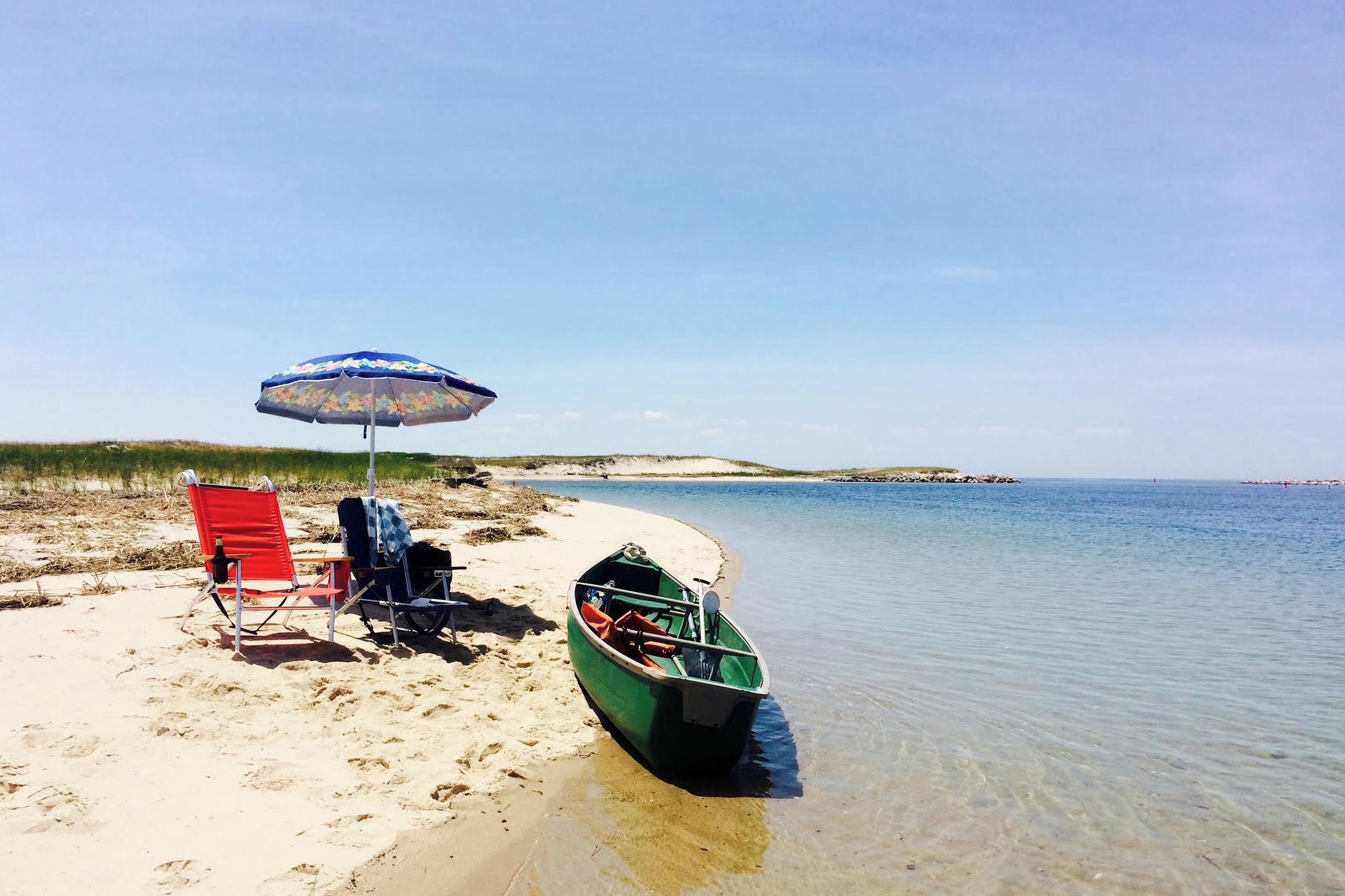 A beach with a boat, a red chair, and a blue umbrella.