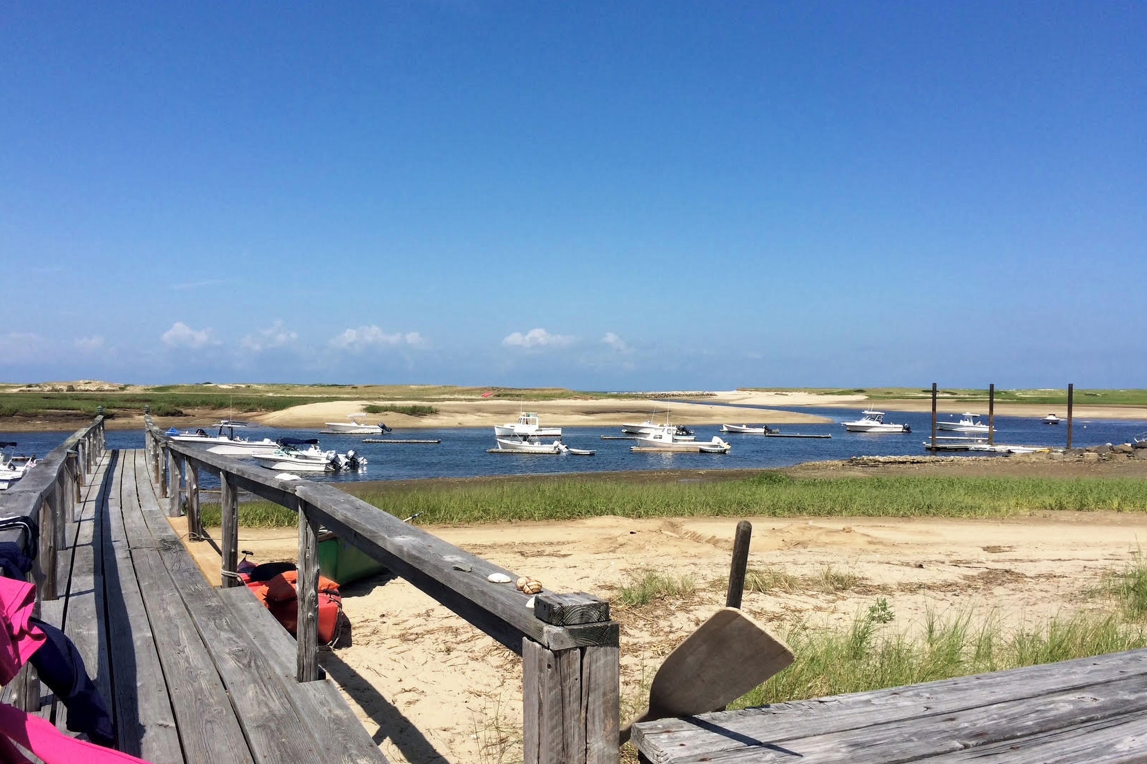 A wooden pier leading to a sandy beach with boats docked in the water.