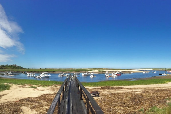 A wooden pier leading to a calm water body with boats, a clear sky, and a distant building on the horizon. - Waterfront Studio w/ Dock & Beach Access in Truro! (Truro)