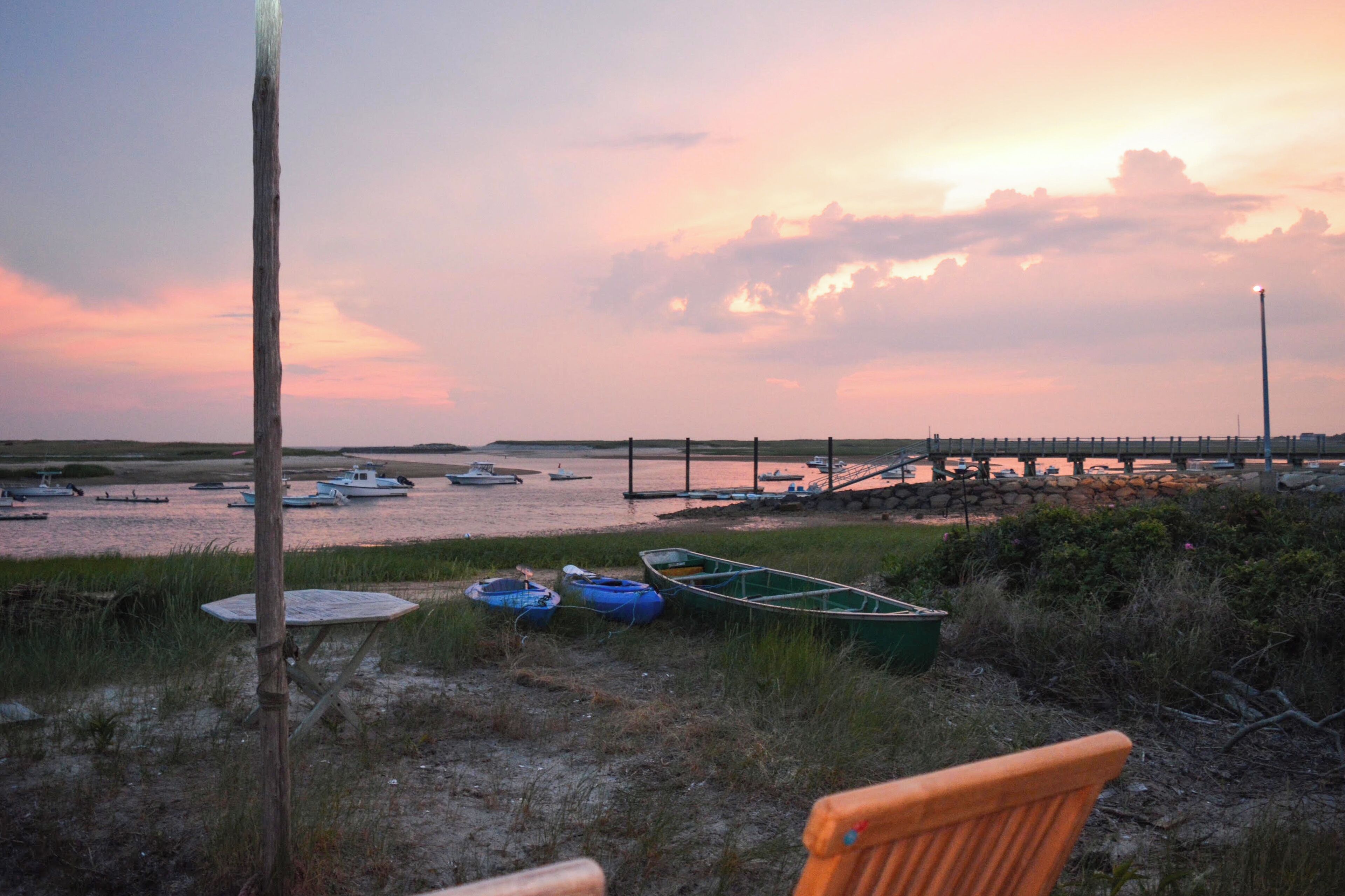 A beach with boats, a wooden pier, and a wooden bench.