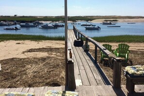 A wooden deck with green chairs and a table, overlooking a calm body of water with boats. - Waterfront Studio w/ Dock & Beach Access in Truro! (Truro)