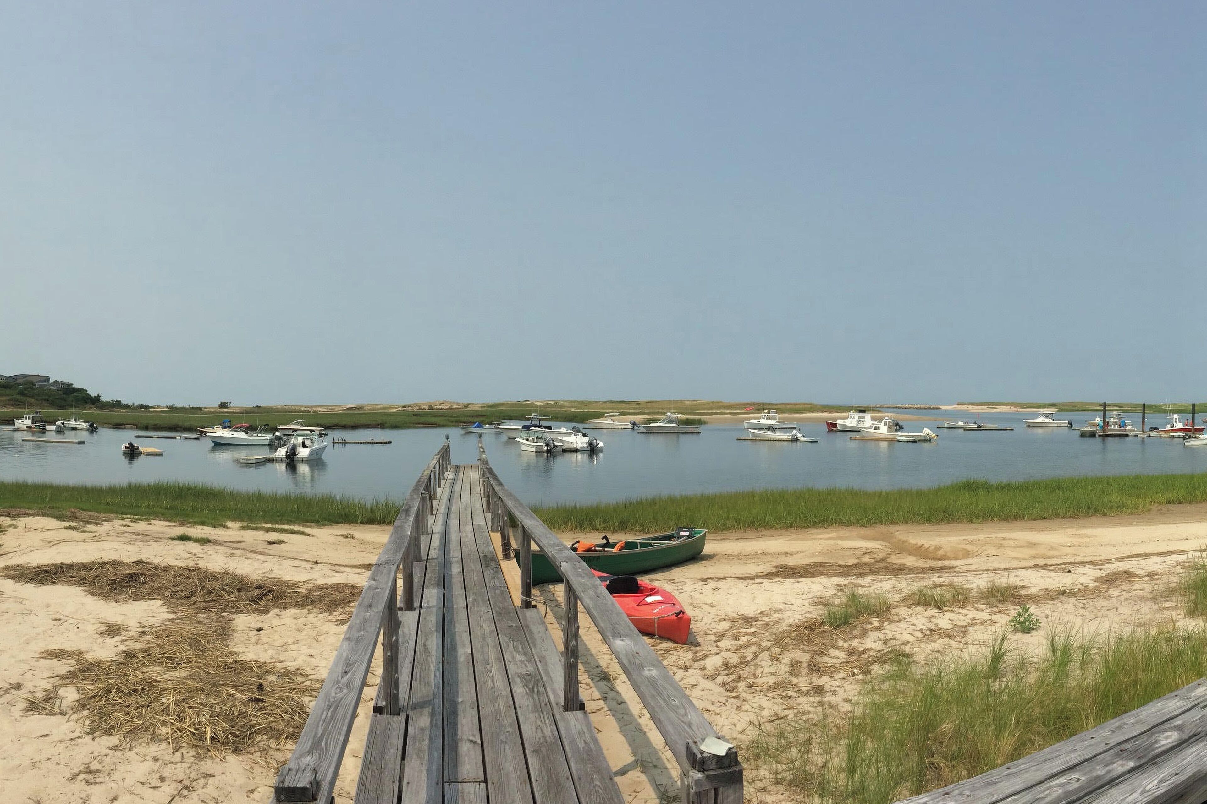 A wooden pier leading to a calm body of water with boats docked.