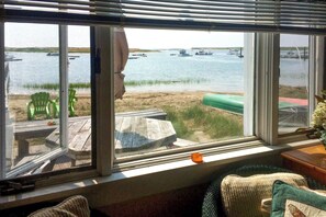 A room with a large window overlooking a body of water with boats, a wooden deck outside, and a green chair inside. - Waterfront Studio w/ Dock & Beach Access in Truro! (Truro)