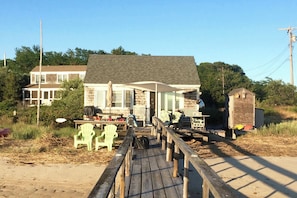 A wooden pier leading to a house with a porch, surrounded by greenery and a clear sky. - Waterfront Studio w/ Dock & Beach Access in Truro! (Truro)