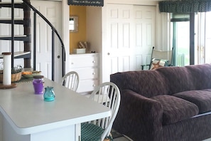 A room with a white table, purple candle, teal candle holder, white chairs, a dark brown sofa, a white dresser, a mirror, and a staircase. - Waterfront Studio w/ Dock & Beach Access in Truro! (Truro)