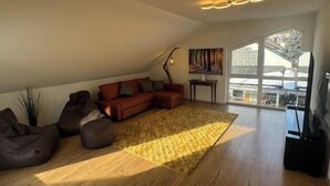 A loft-style living room with a wooden floor, a sectional sofa, a coffee table, a floor lamp, and a painting on the wall. - Vacation apartment Schwarzwaldblick Unterkirnach (Unterkirnach)