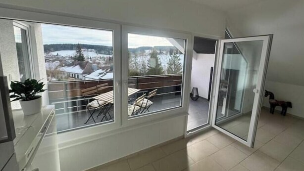 A balcony with a view of a snowy landscape, a sliding glass door, and a potted plant. - Vacation apartment Schwarzwaldblick Unterkirnach (Unterkirnach)