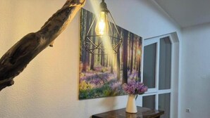 A room with a wooden floor, a painting of a forest, a table with a vase of flowers, and a hanging light fixture. - Vacation apartment Schwarzwaldblick Unterkirnach (Unterkirnach)