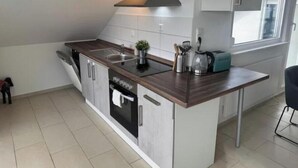 A modern kitchen with a built-in stove, sink, and dishwasher, a small island with a toaster, and a window providing natural light. - Vacation apartment Schwarzwaldblick Unterkirnach (Unterkirnach)