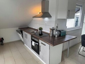 A modern kitchen with a built-in stove, sink, and dishwasher, a small island with a toaster, and a window providing natural light. - Vacation apartment Schwarzwaldblick Unterkirnach (Unterkirnach)