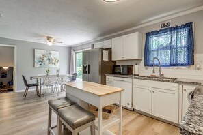 A modern kitchen with white cabinets, a granite countertop, and a dining area with a table and chairs. - Easy ATL Access! Suburban Retreat w/ Yard & Patio (Riverdale)