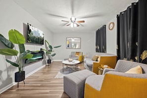 A modern living room with a ceiling fan, a flat-screen TV, a sofa, a coffee table, and potted plants. - Easy ATL Access! Suburban Retreat w/ Yard & Patio (Riverdale)