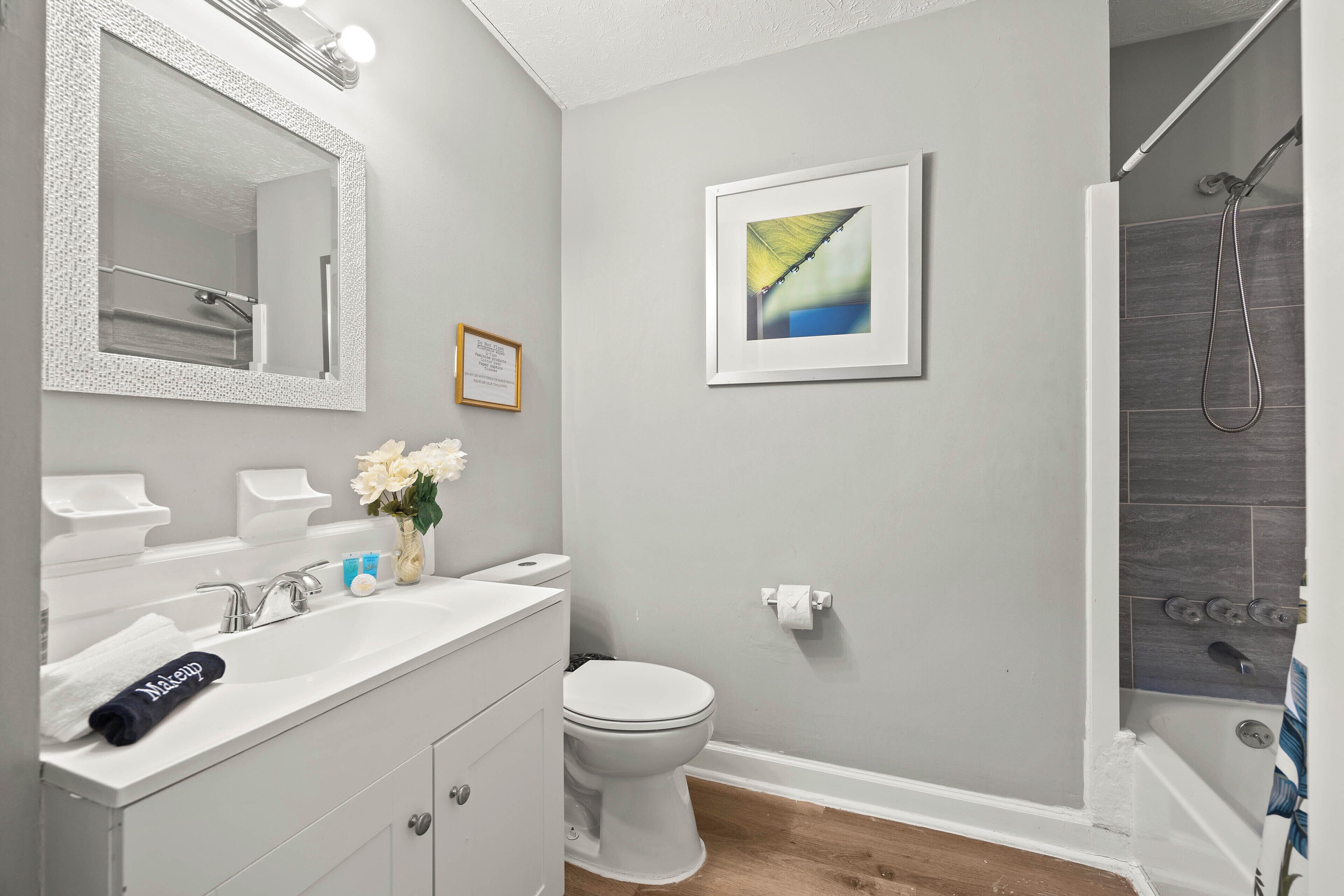 A bathroom with a white vanity, a toilet, a shower, and a framed abstract painting on the wall.