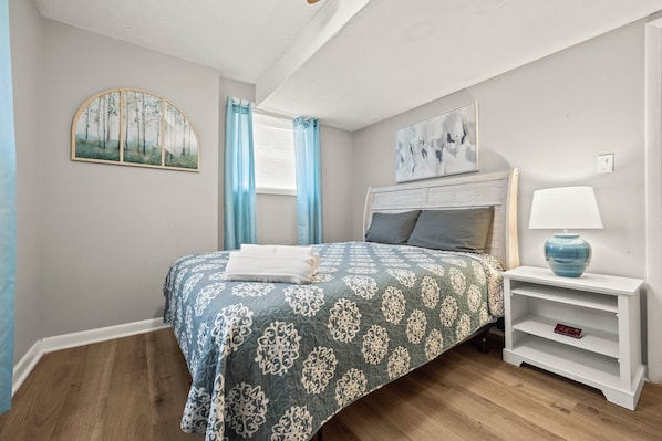 A bedroom with a bed, a nightstand, a lamp, a painting, and a window with curtains. - Easy ATL Access! Suburban Retreat w/ Yard & Patio (Riverdale)