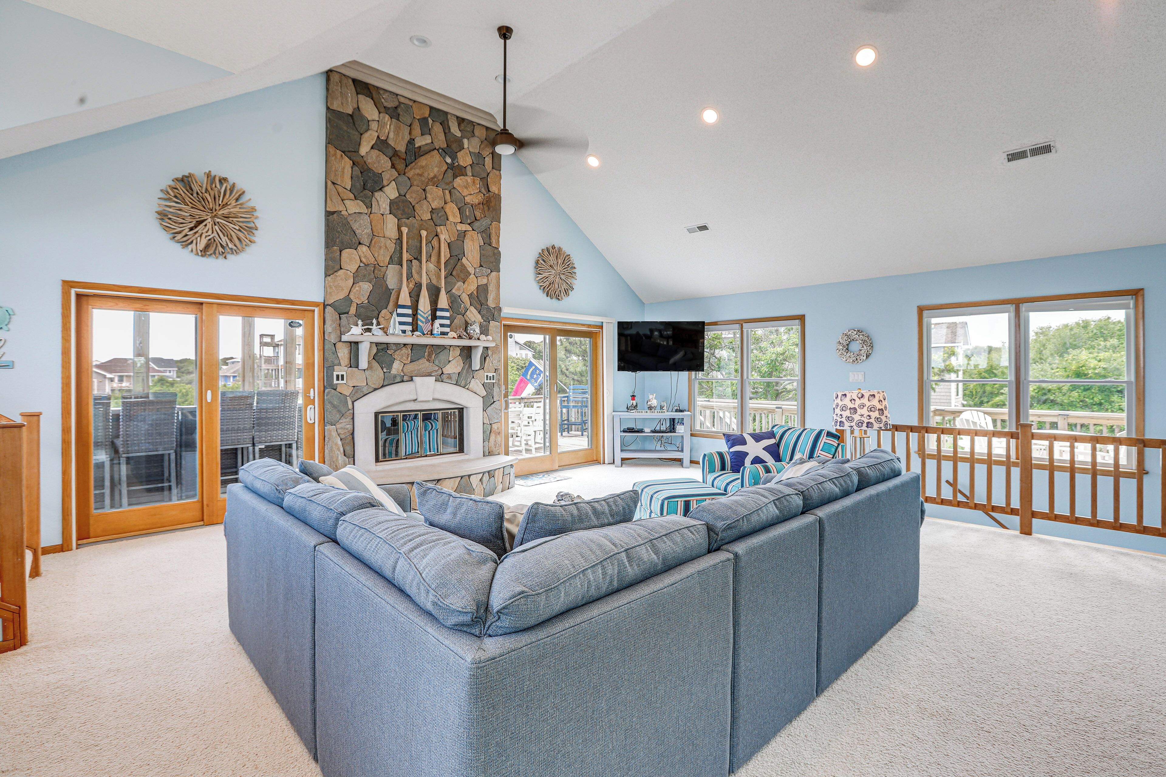 A living room with a stone fireplace, a large gray sectional sofa, and a TV mounted on the wall.
