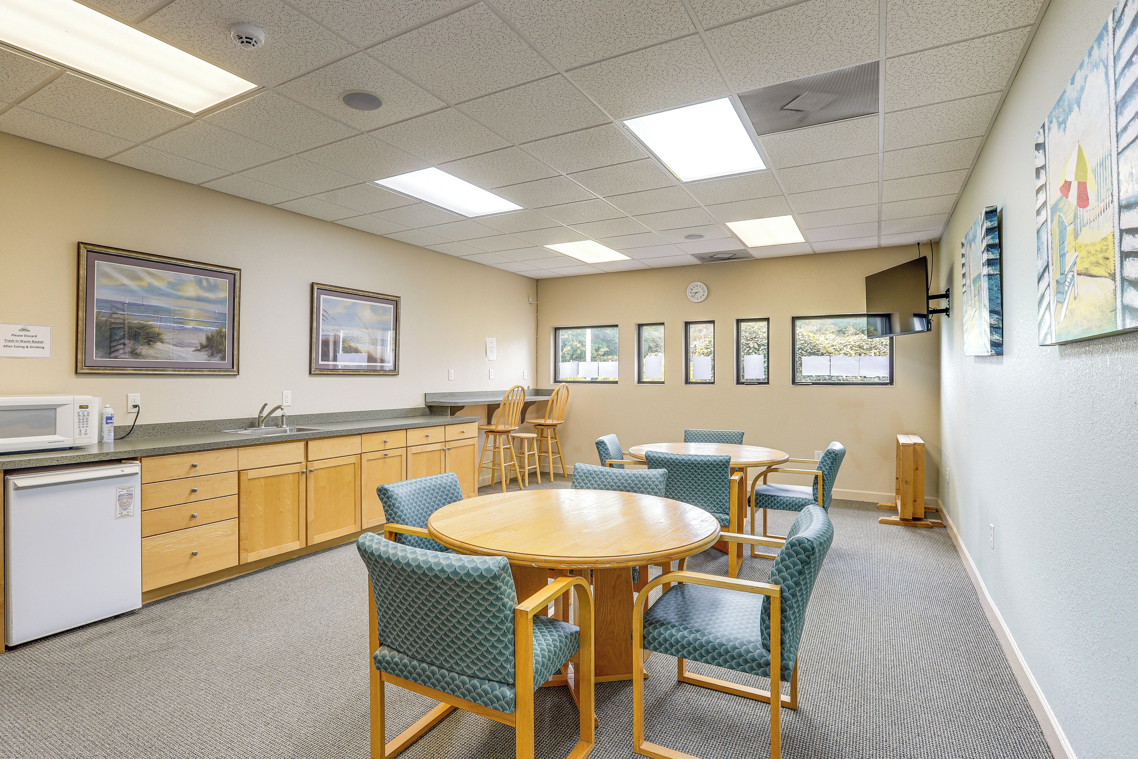 A kitchen with a microwave, sink, and cabinets, a dining area with chairs and a table, and artwork on the walls.