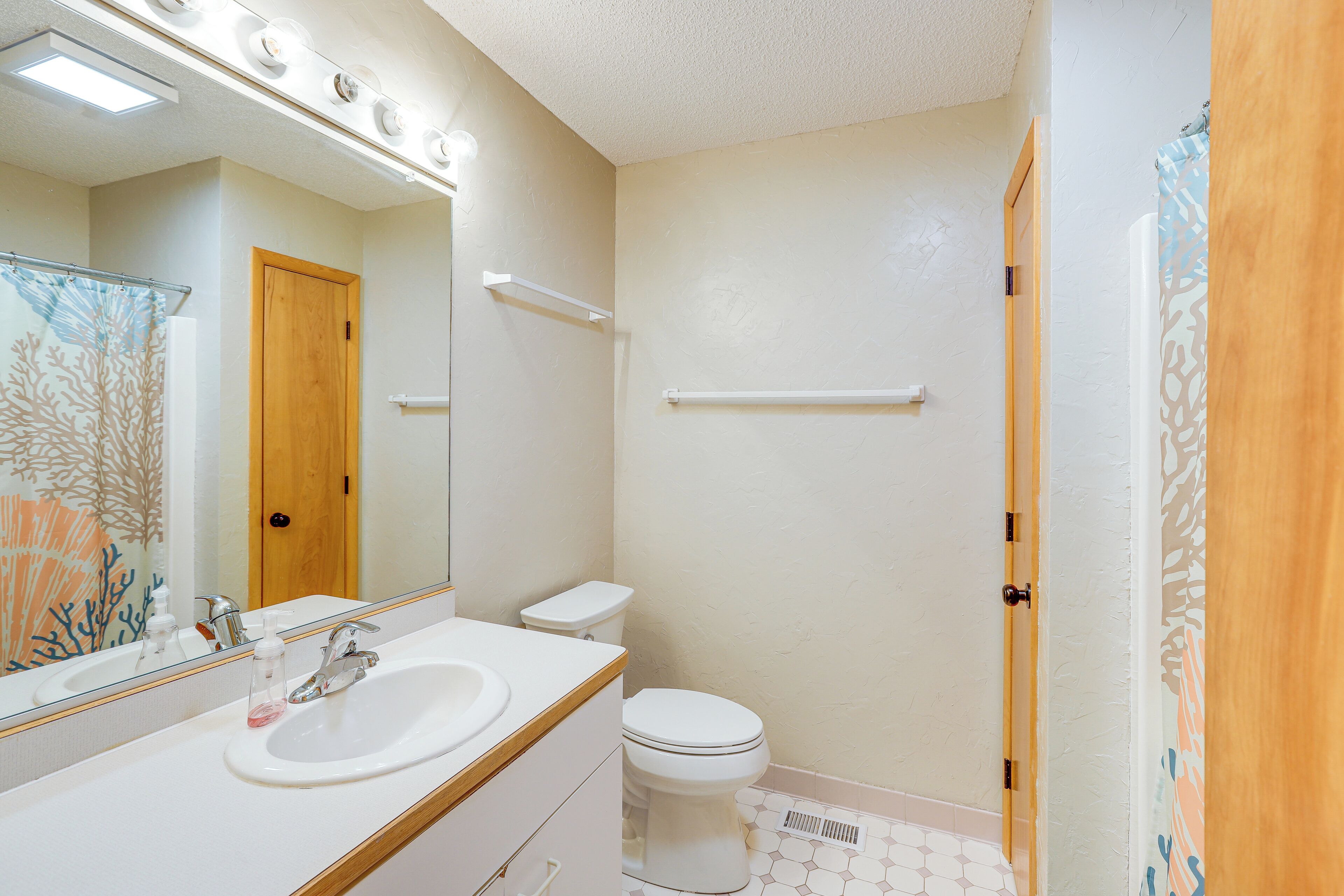 Un baño con lavamanos, espejo, inodoro y cortina de ducha.