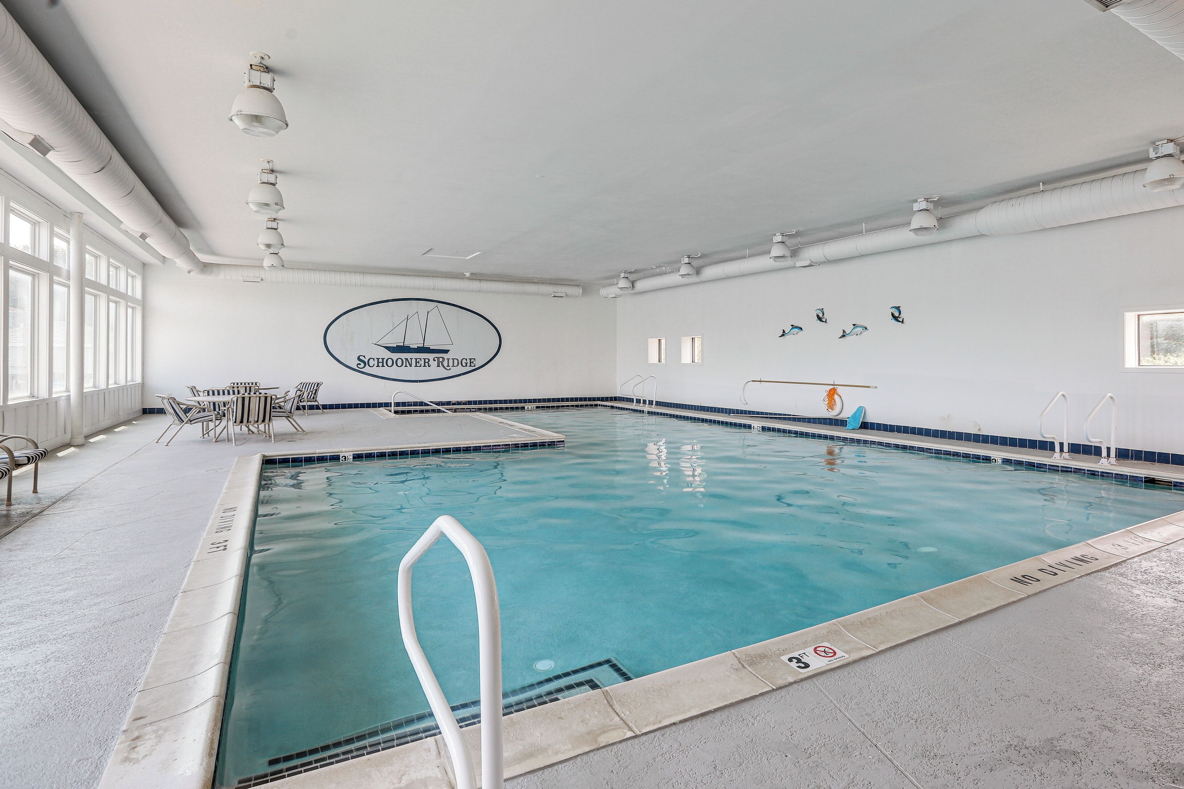 An indoor swimming pool with clear water, a pool ladder, and a logo on the wall.