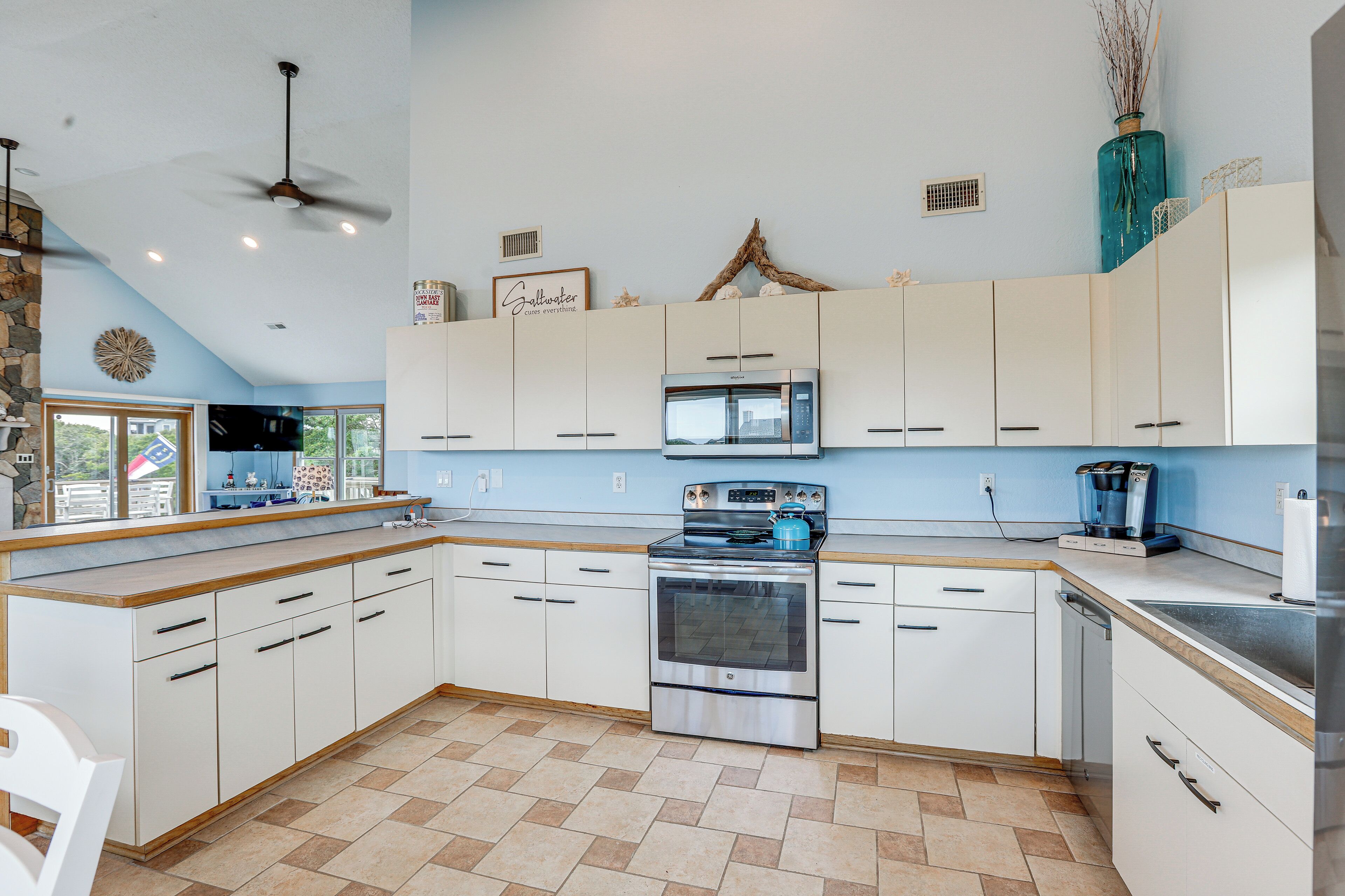 A kitchen with white cabinets, a stove, an oven, a microwave, and a ceiling fan.