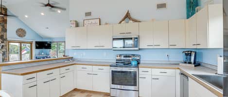 A kitchen with white cabinets, a stove, an oven, a microwave, and a ceiling fan.