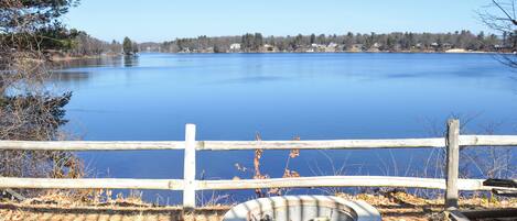 A calm lake with a wooden fence and a fire pit in the foreground.