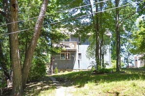 A two-story building with a wooden exterior, surrounded by trees and a pathway leading to the entrance.