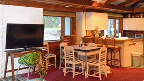 A dining area with a TV, chairs, a table, and a kitchen area with a microwave.