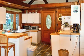 Una cucina compatta con mobili bianchi, un forno a microonde, una macchina per il caffè e una porta di legno con vetrata.