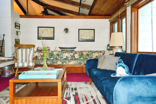 A living room with a wooden coffee table, a blue sofa, a floral sofa, a chair, and a lamp.