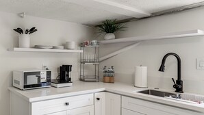Ett modernt kök med vita köksskåp, en mikrovågsugn, en kaffebryggare och en diskho.