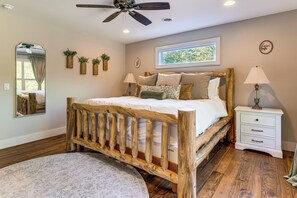 Un dormitorio con cama de madera, una mesita de noche, una lámpara, un espejo y una ventana con vistas a la vegetación.