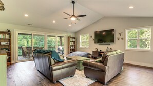 A spacious living room with leather sofas, a flat-screen TV, and a large window overlooking a deck.