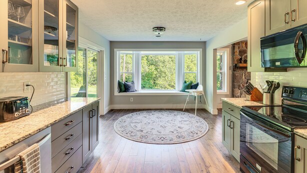 A kitchen with a built-in stove, a window seat, and a view of greenery outside.