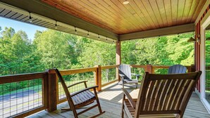 A wooden deck with rocking chairs and a table, overlooking a forested area.