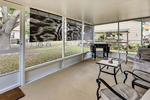 Un patio cubierto con mesa y sillas, una parrilla y vista a un jardín trasero con un árbol y una cerca.