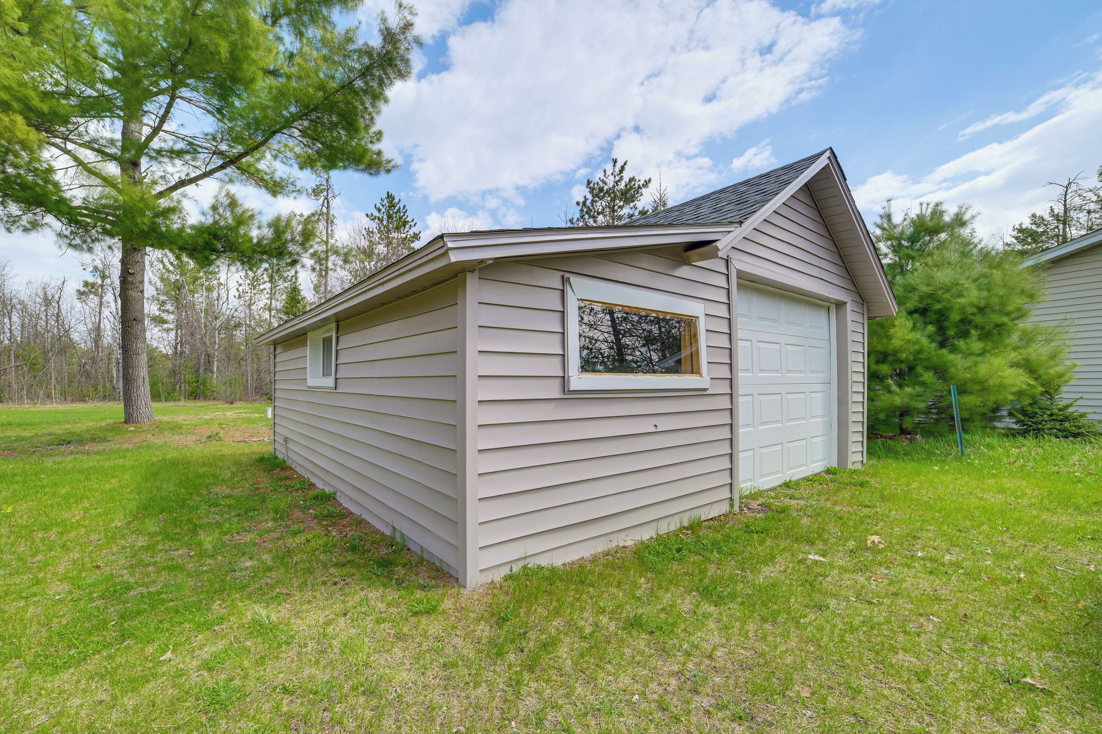 A single-story, light-colored wooden cabin with a garage, a small window, and a sloped roof.