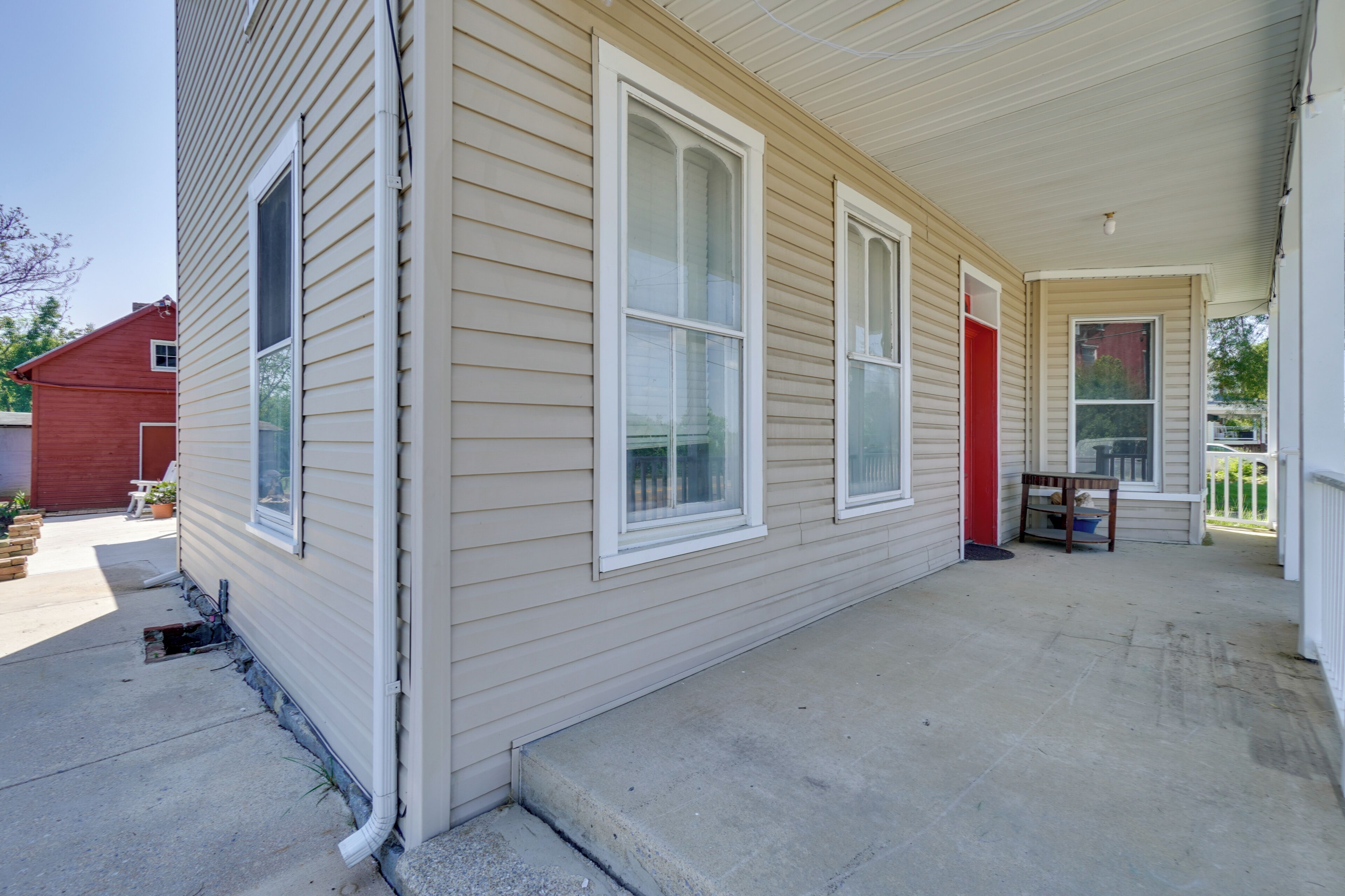 A residential building with a covered porch, large windows, and a red door.