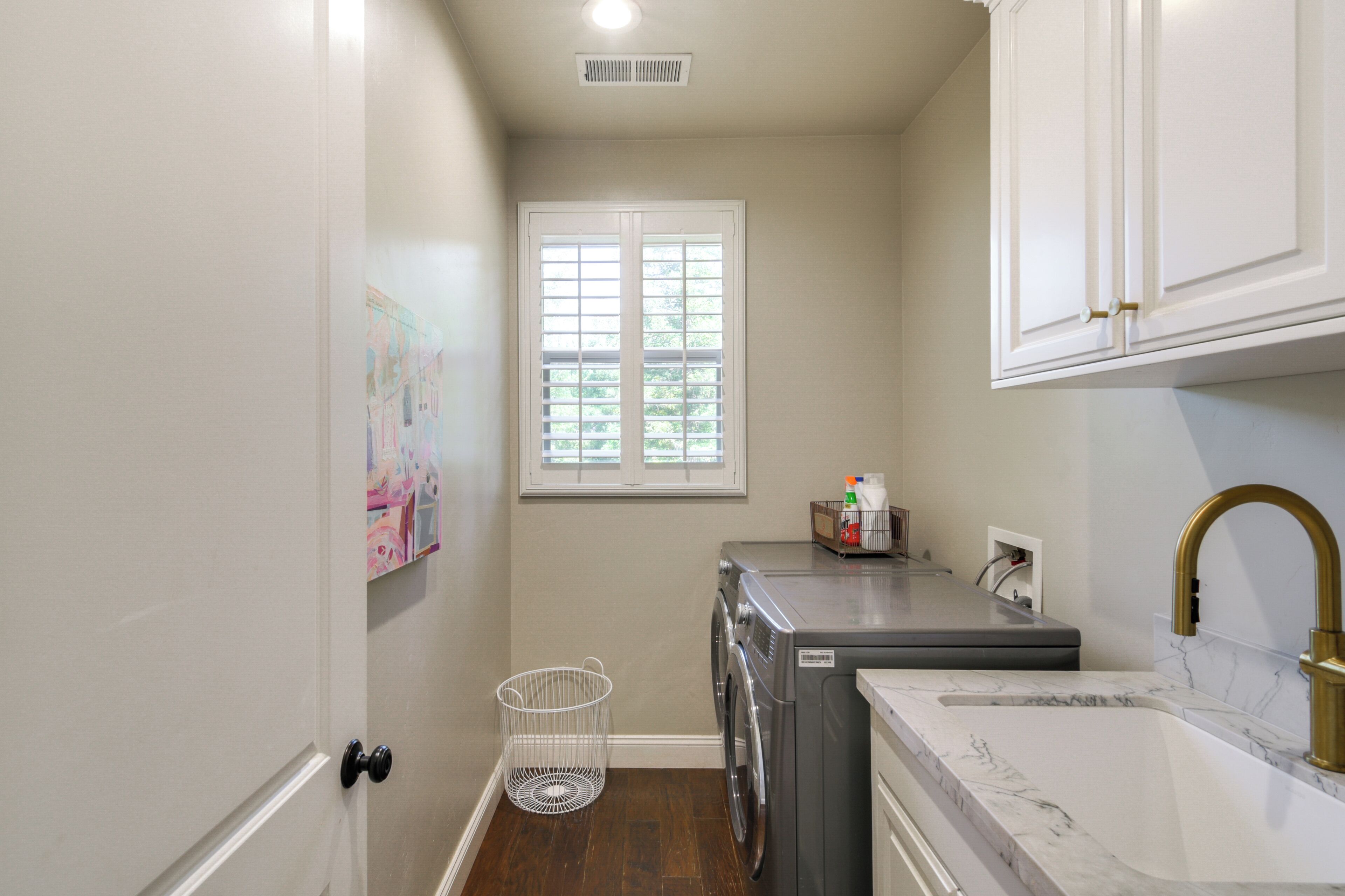 A laundry room with a washing machine, a sink with a gold faucet, a window, and a door.