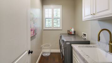 A laundry room with a washing machine, a sink with a gold faucet, a window, and a door.
