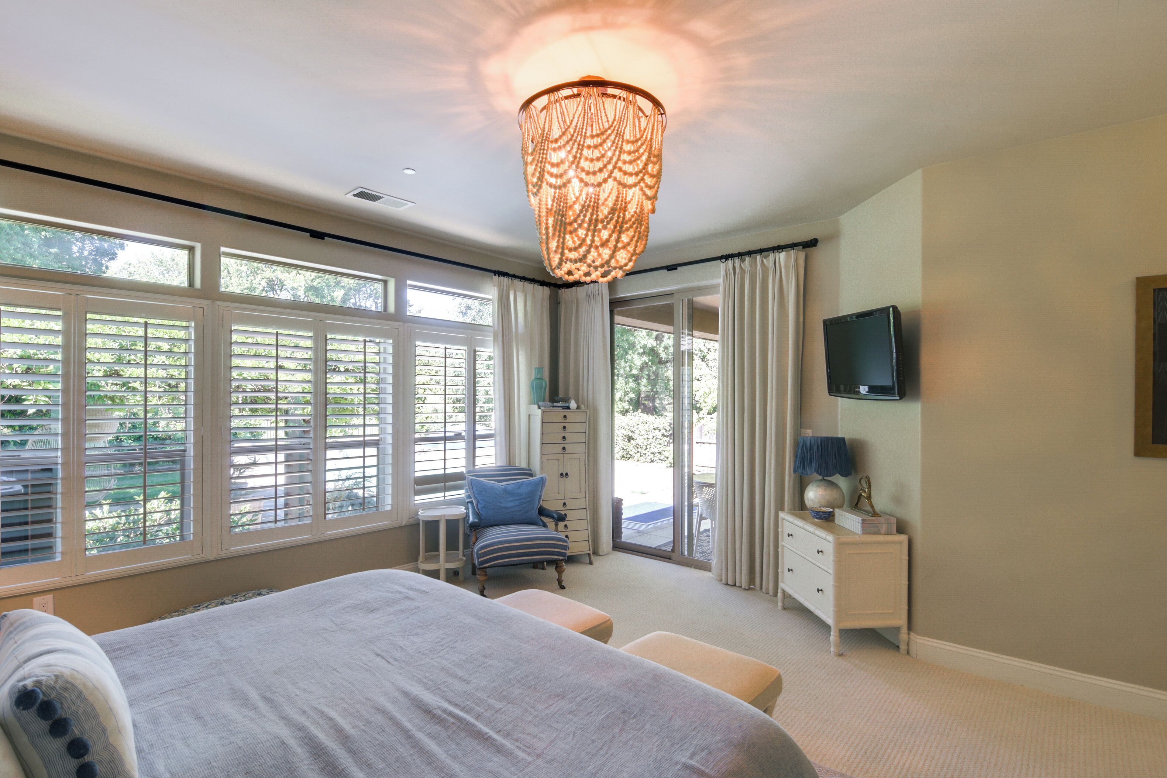 A bedroom with a bed, a chair, a dresser, a television, and large windows.