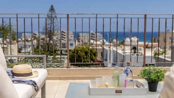 A balcony with a white sofa, a hat, a tray with drinks, and a potted plant.