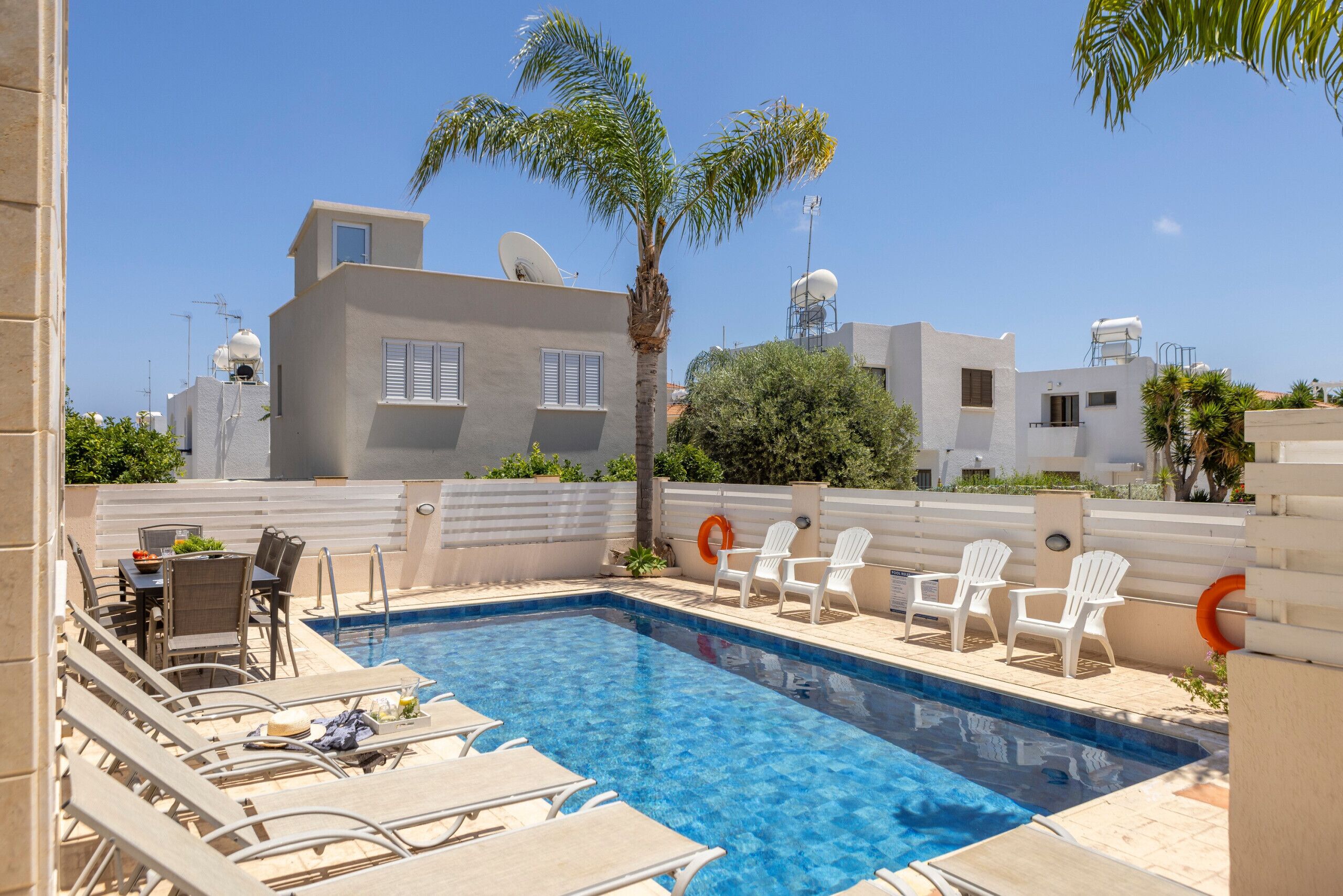 A swimming pool with lounge chairs, a table, and a palm tree.