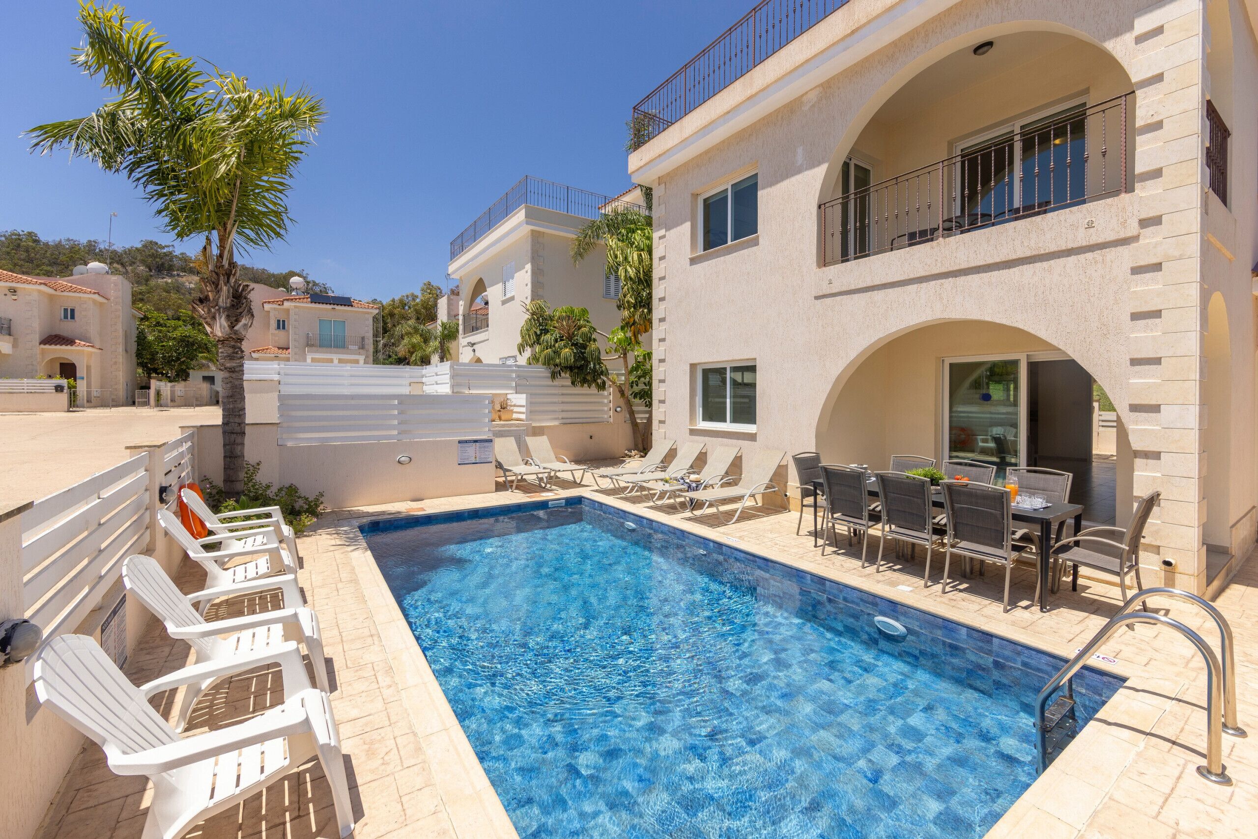 Une piscine entourée de bâtiments dotés de balcons, avec des chaises longues et un espace repas à proximité.