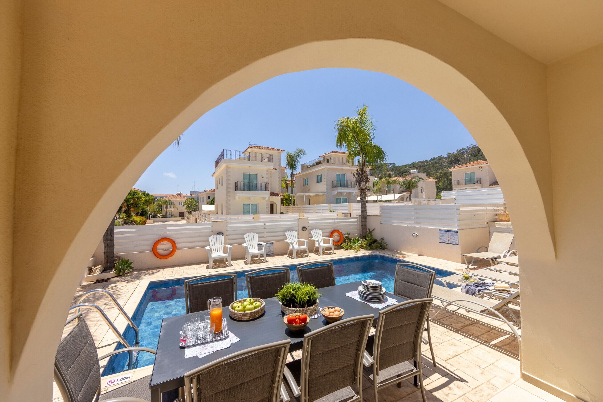 A poolside dining area with a table set for two, a pool, and a view of buildings in the background.
