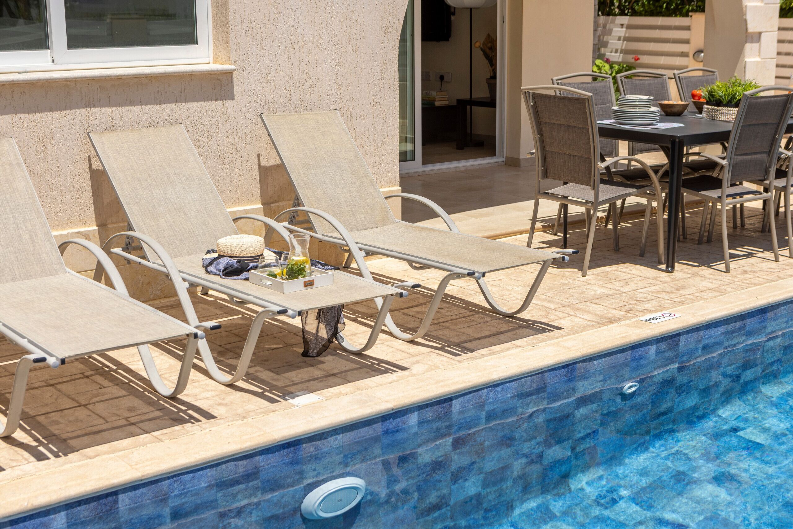 A poolside area with lounge chairs, a table, and a dining set.