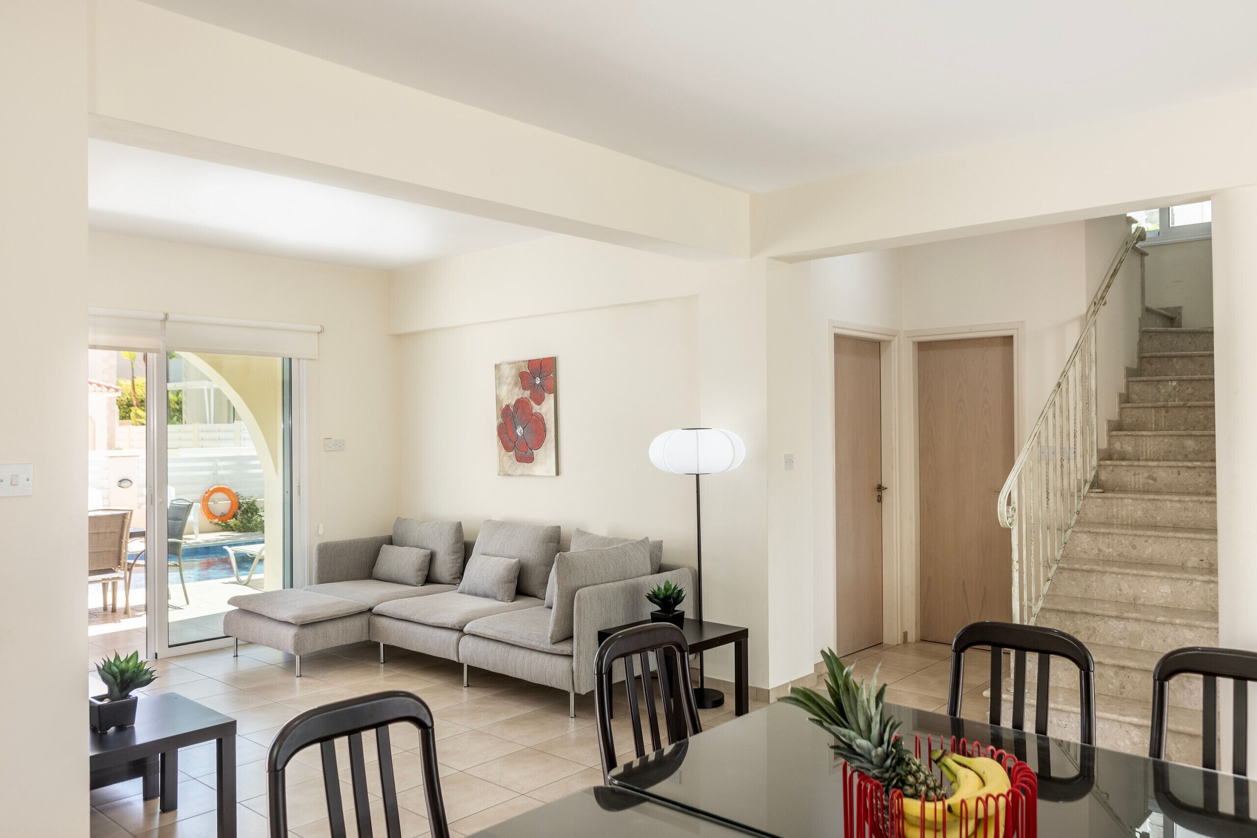Un salon comprenant un canapé d’angle, une table à manger avec des chaises, un escalier et une piscine visible à travers une porte vitrée.