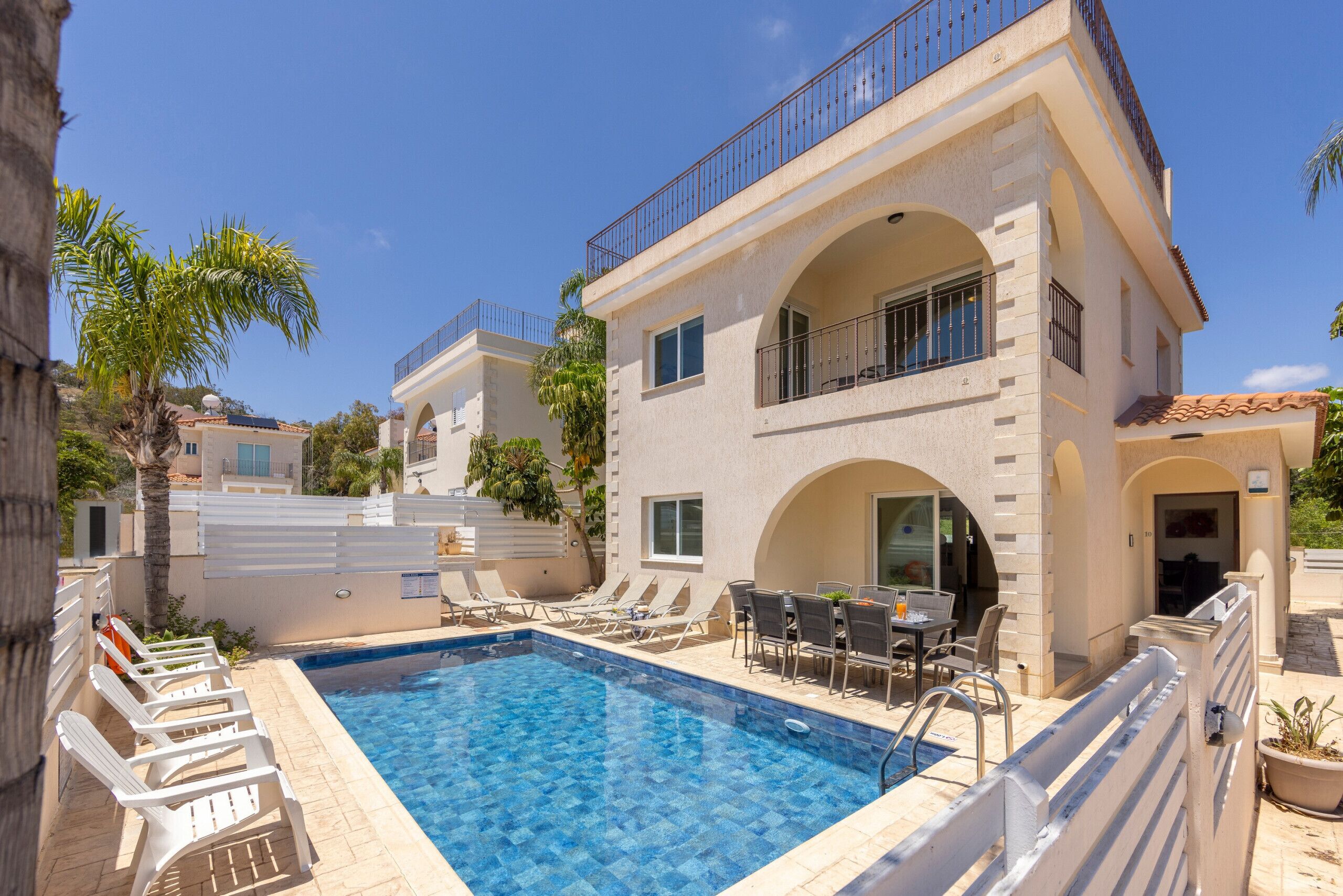 A poolside area with lounge chairs, a dining table, and a two-story building with balconies.